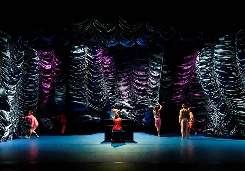 Stor scen med böljande tyger, en klassisk pianist är omringad av dansare i den samtida dansföreställningen Pianofavoriter med Norrdans. Foto: Lia Jacobi