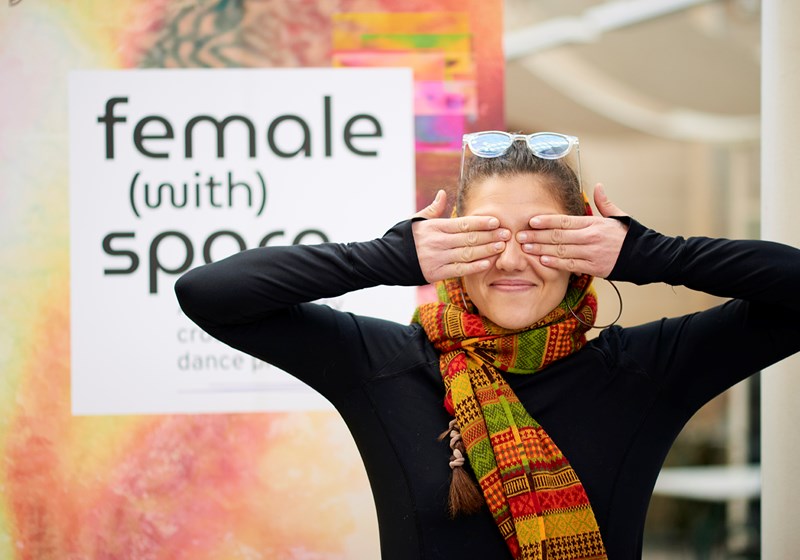 Koreografen Polena Kolia Petersen håller för ögonen framför affisch för Norrdans community projekt Female (with) Space