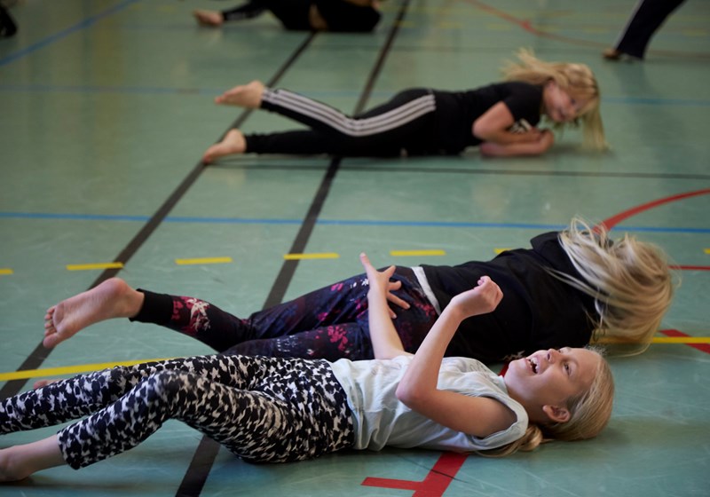 Unga tjejer skrattar och rullar på golvet under dansworkshop med danskompaniet Norrdans.