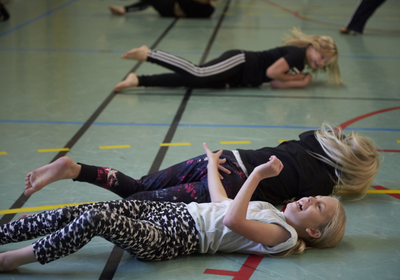 Unga tjejer skrattar och rullar på golvet under dansworkshop med danskompaniet Norrdans.