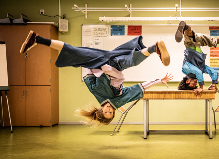 A person crouches amid a tangle of hands and pencils.